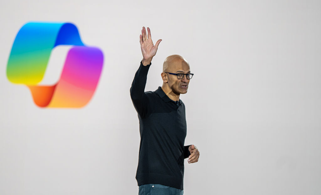 Microsoft CEO Satya Nadella waves during an event celebrating the 50th Anniversary of Microsoft with a Copilot logo in the background