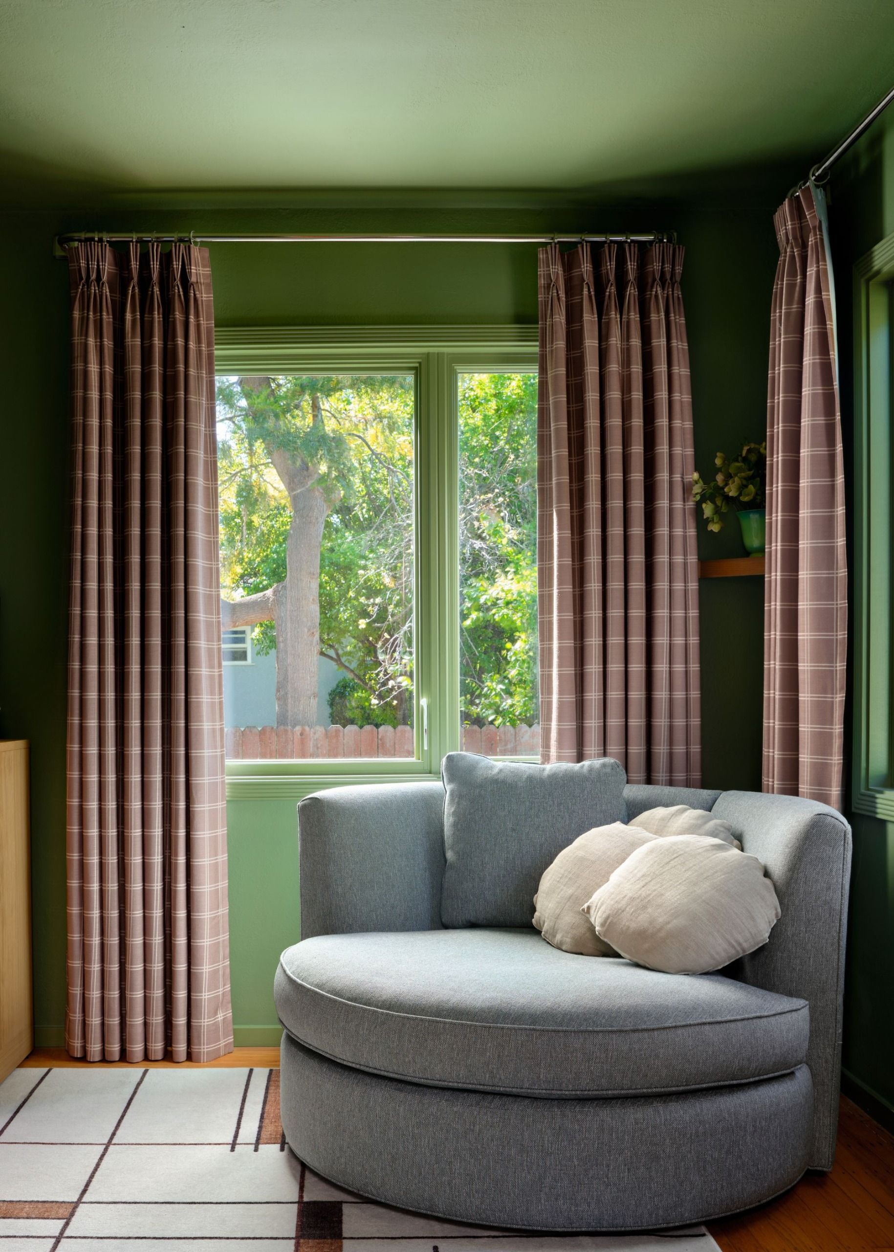 A bedroom with teal walls, grey armchair and chequered curtains