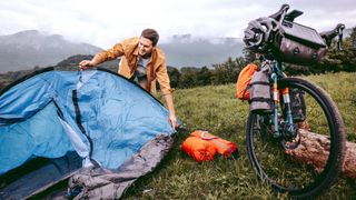 Bikepacker setting up tent in field