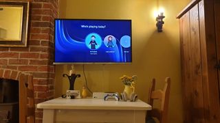 Wall mounted TV showing Xbox sign in screen and Xbox Series S console on table in a cottage