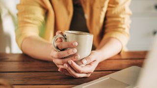 Woman's hands holding a mug over wooden table