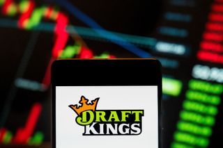 draftkings logo on smartphone with stock chart blurred in background