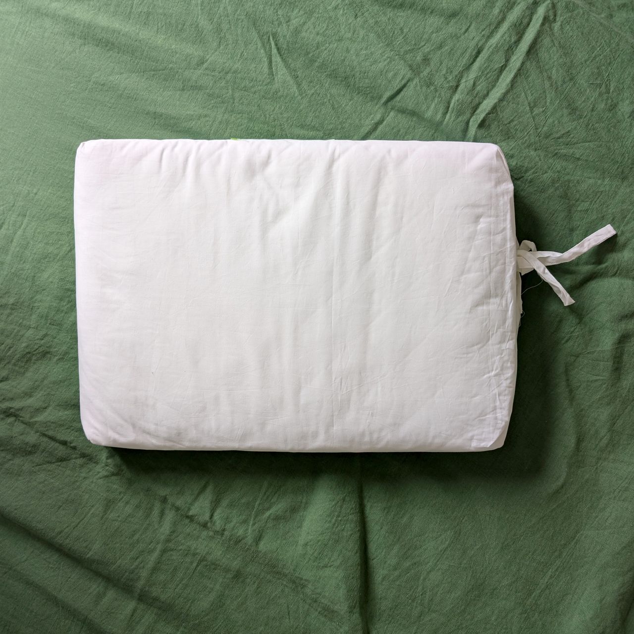 Scooms mattress protector folded up in a white cotton bag on top of a green bed.