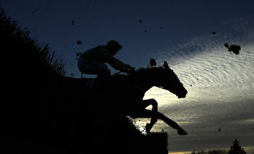 In silhouette, a horse and jockey jumping over a hedge during the steeple chase at Kempton Park