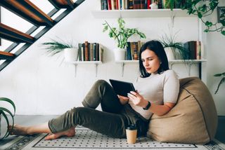 Young woman relaxing on a beanbag and using a tablet device.