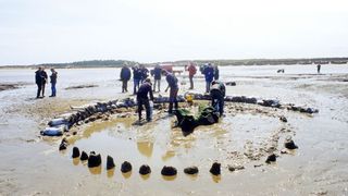 people in a sandy marsh, near a circle of stones sticking out of the surface.