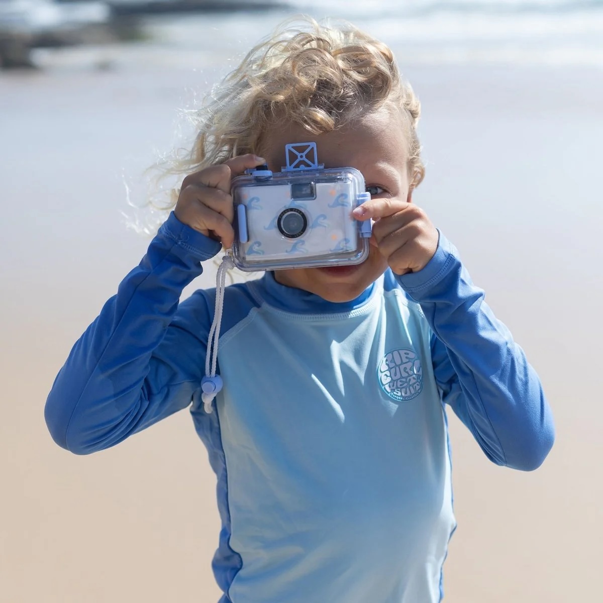 Child in a blue rash vest holding an underwater camera