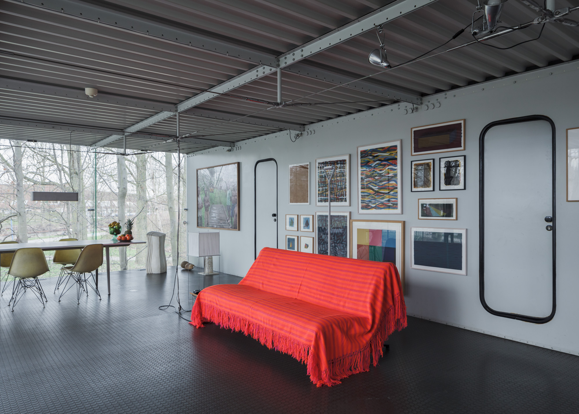 the living and dining room of the space. there is a red sofa in the middle of the space. floor-to-ceiling windows give the space light.
