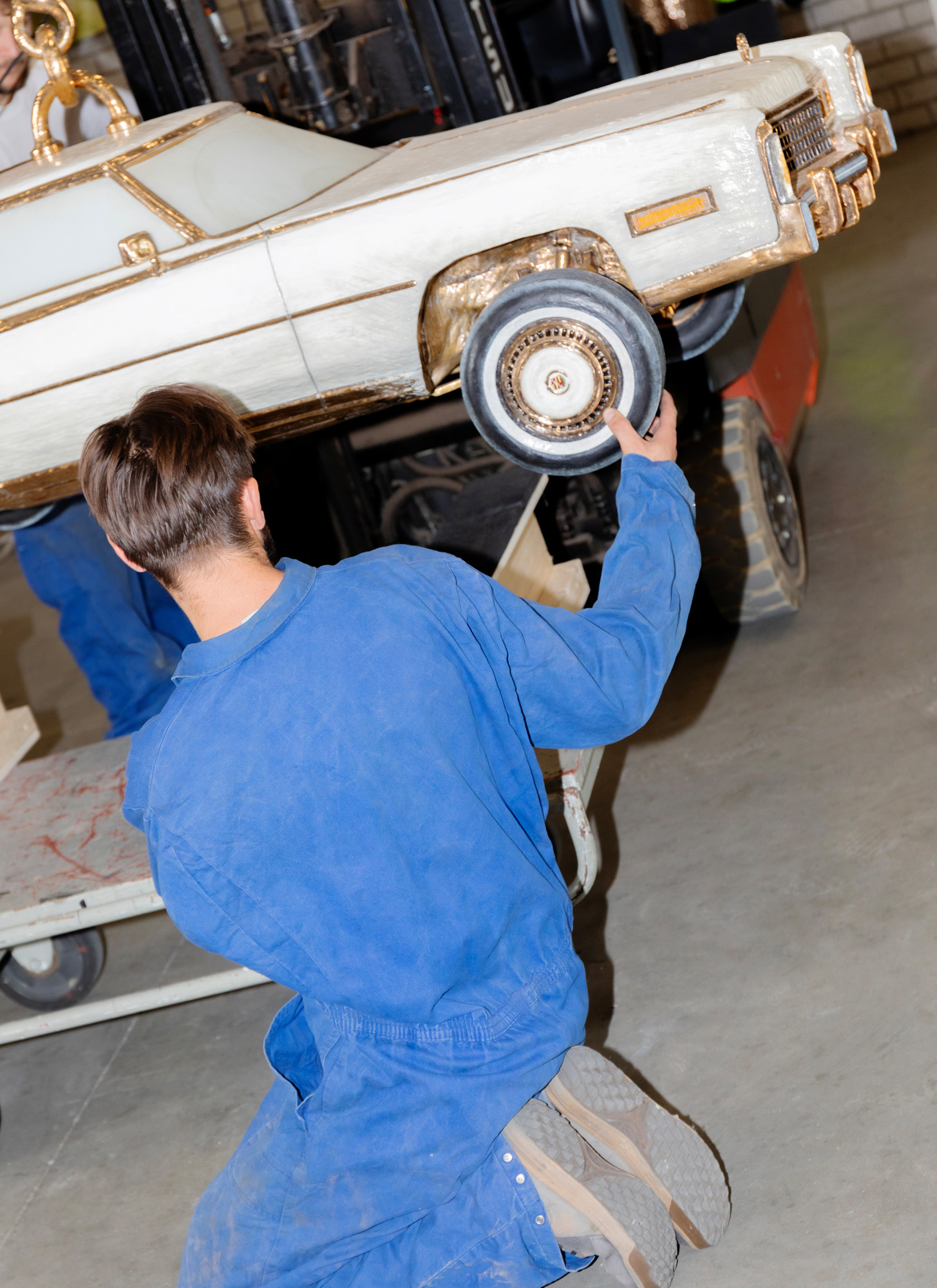 A person wearing blue overalls, photographed from the back and working on a white car model inside Studio Job&#039;s Tilburg workshop