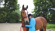 A girl holding and half hugging a bay horse