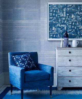 blue bedroom corner with blue wallcover, blue armchair, chest of drawers and blue geometric artwork