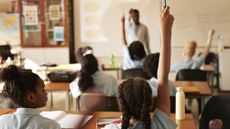 Kids in a classroom, some with their hands raised to answer a question.