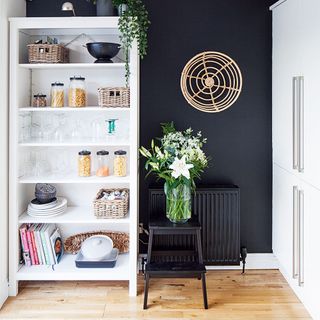 kitchen area with black wall white cabinets white shelve and flower vase on table