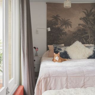 White bedroom with large fabric headboard with palm trees on it and a cat sitting on the bed