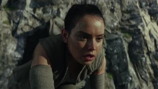 Rey crouches in front of a cliff on Ahch-To in The Last Jedi.