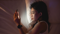 Asian woman using mobile phone smartphone laying on the bed in the bedroom. Sleepy exhausted, can not sleep. Insomnia, addiction concept. Women scrolling social networks on mobile dark bedroom.