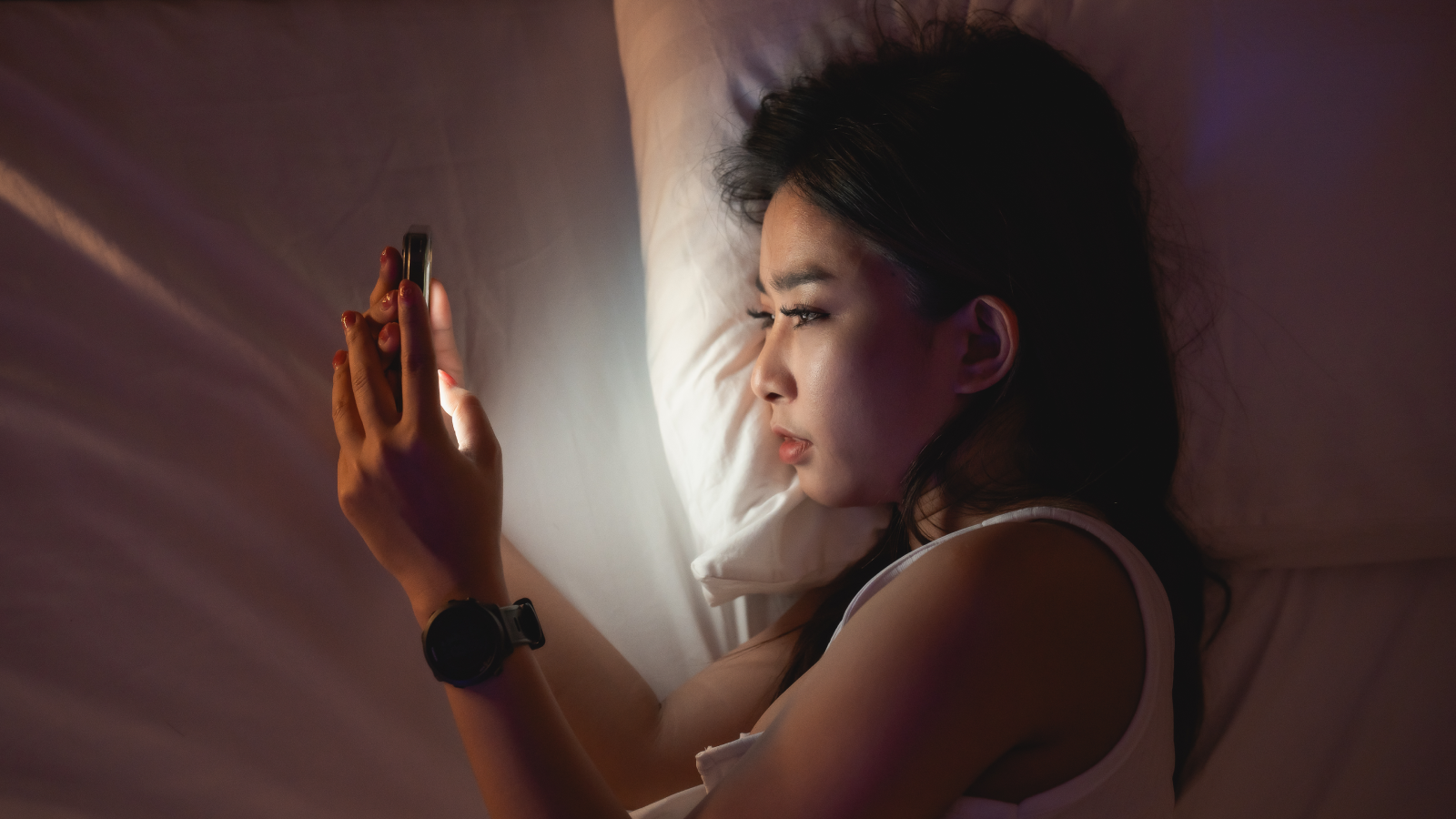 Asian woman using mobile phone smartphone laying on the bed in the bedroom. Sleepy exhausted, can not sleep. Insomnia, addiction concept. Women scrolling social networks on mobile dark bedroom.