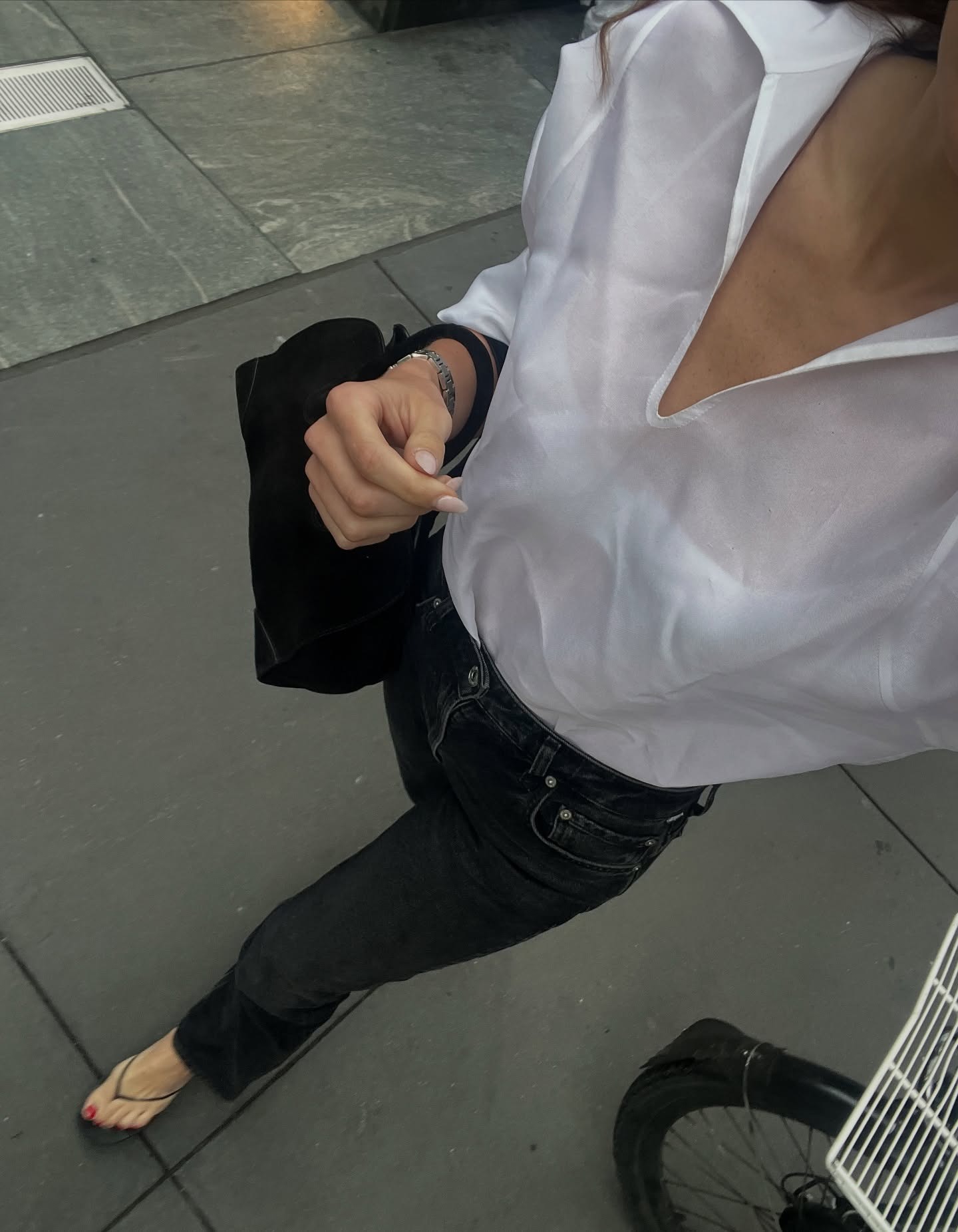 Eliza Huber wearing a white top, black high-waisted jeans, and heeled thong sandals.