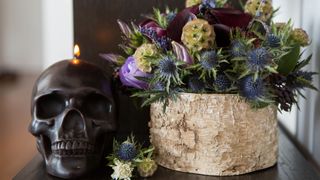 Dark flower arrangement next to skull candle holder and lit candle