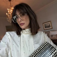 A woman taking a selfie wearing oversized glasses with a long, serrated bob and fringe
