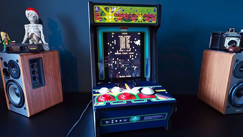 Arcade Classics Centipede arcade machine on black desk next to woodgrain speakers.