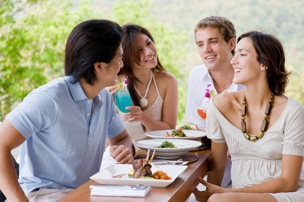 A group of young adults sits around a table, laughing and eating.