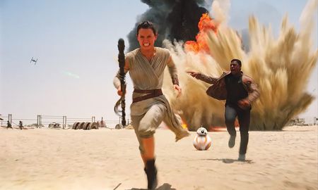 In a scene from The Force Awakens, Rey and Finn sprint across a desert landscape while escaping a massive explosion with BB-8 following closely behind them