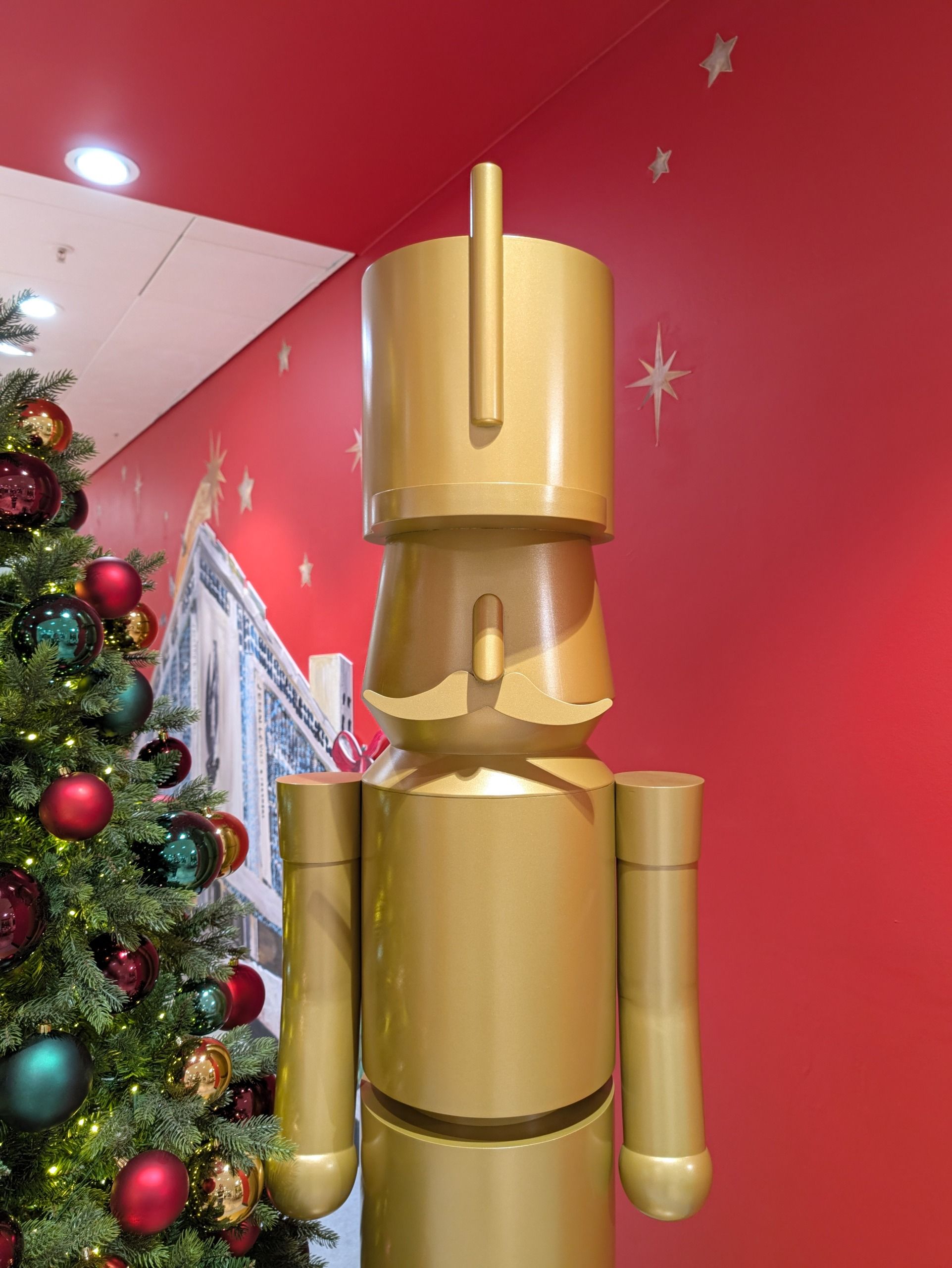 Large gold nutcracker-style Christmas figure standing beside a decorated Christmas tree against a red wall.