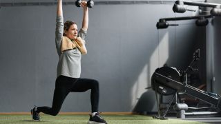Woman performs overhead dumbbell walking lunge