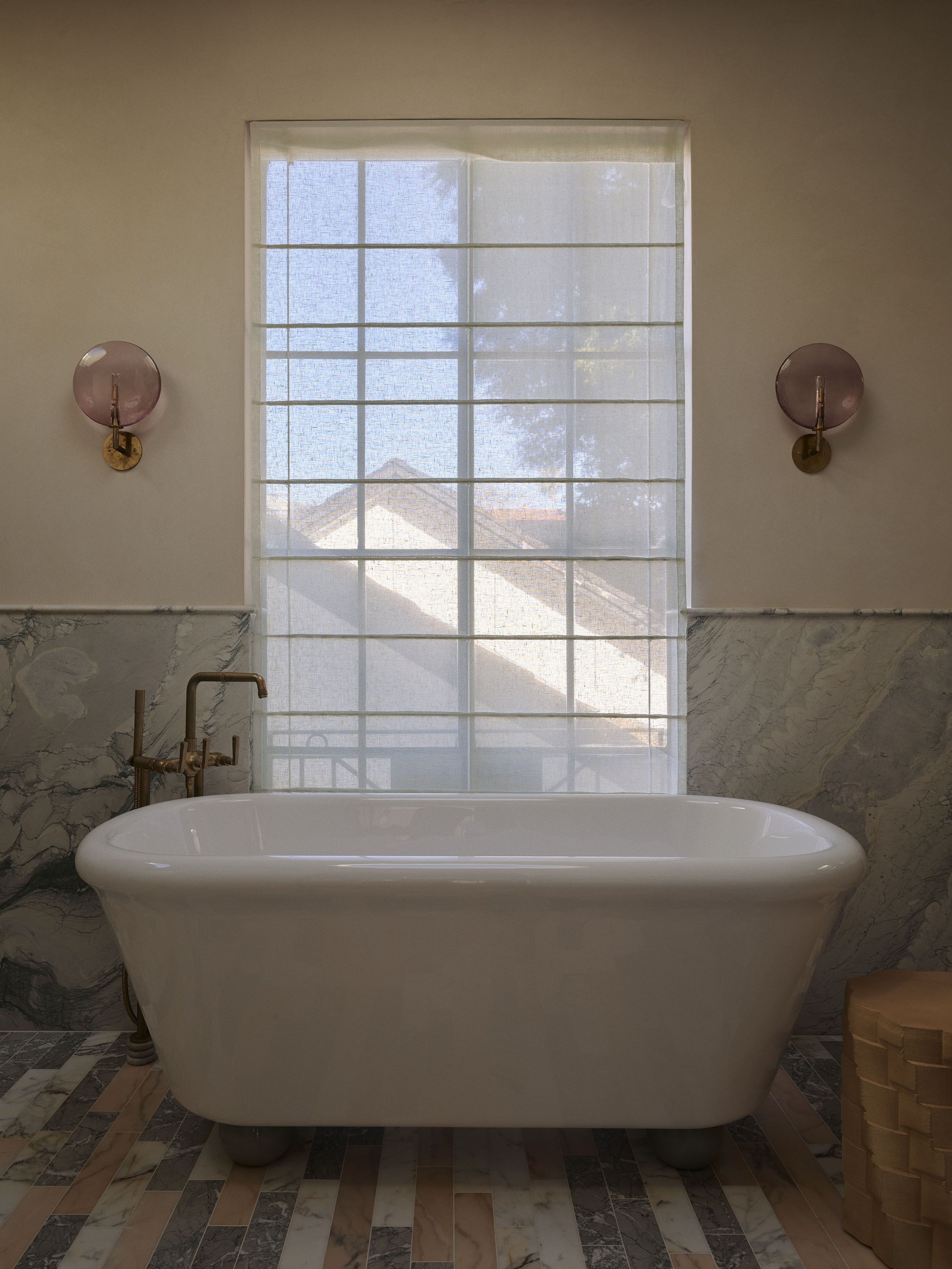 Freestanding bathtub set against a softly filtered window with pink glass wall lights and marble flooring in Smac Studio's renovated Art Deco home in Sydney