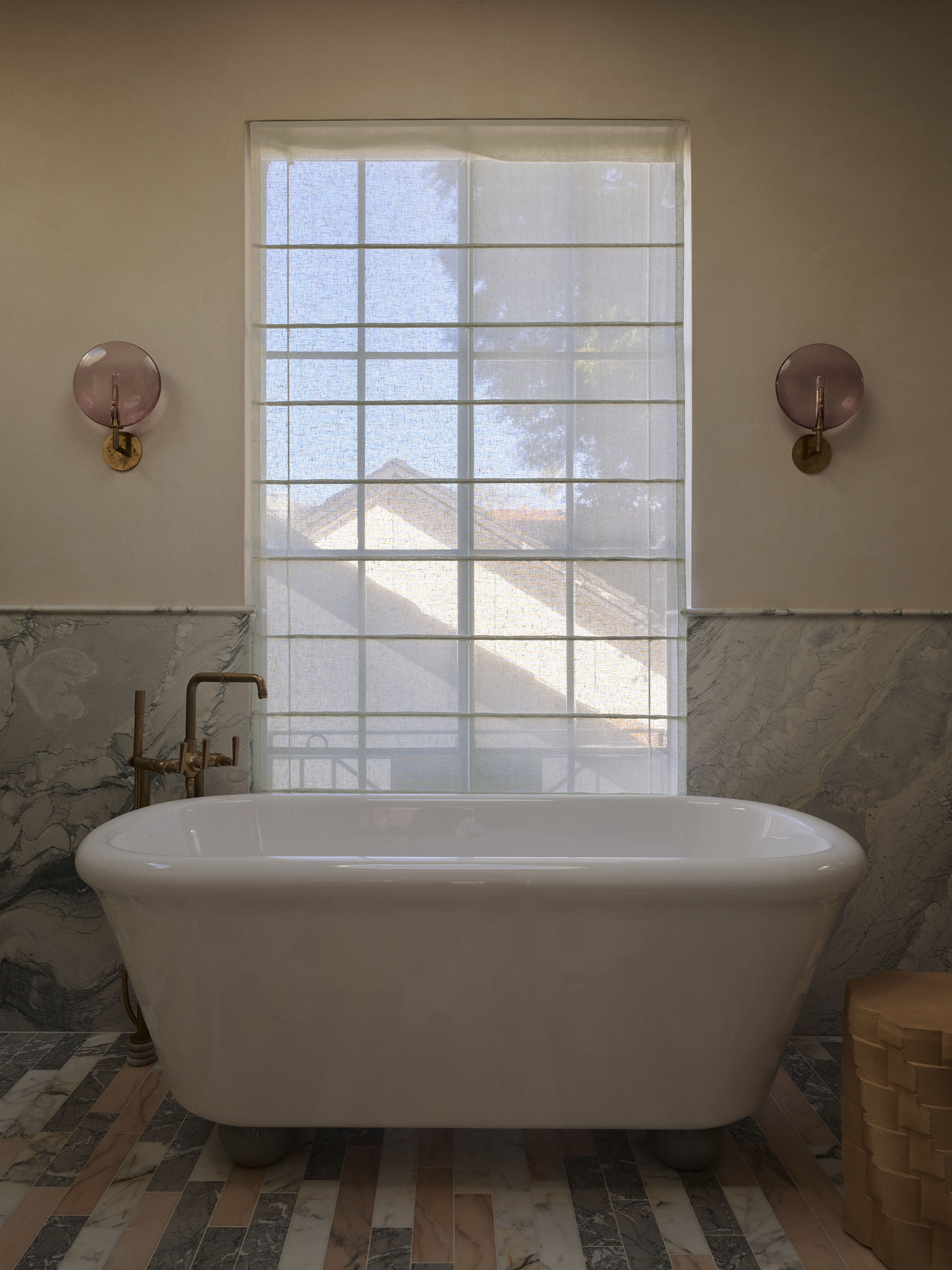 Freestanding bathtub set against a softly filtered window with pink glass wall lights and marble flooring in Smac Studio's renovated Art Deco home in Sydney