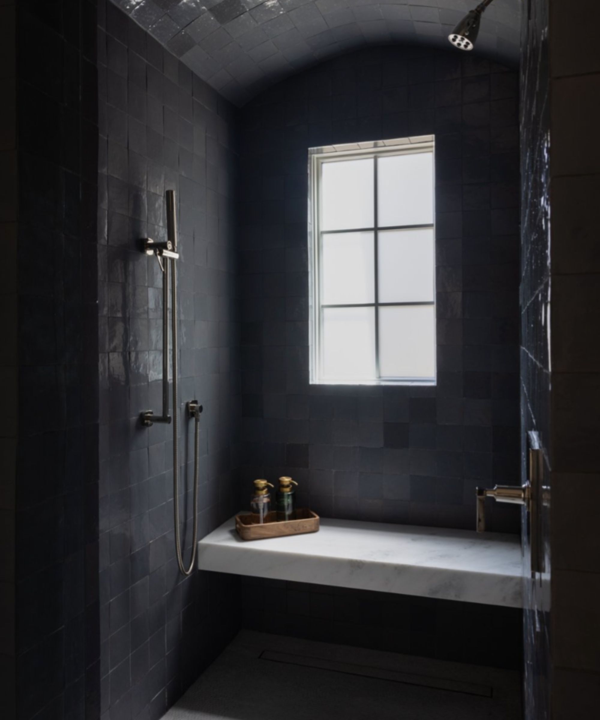 A moody minimalist bathroom tile drenched in black tiles with a marble bench