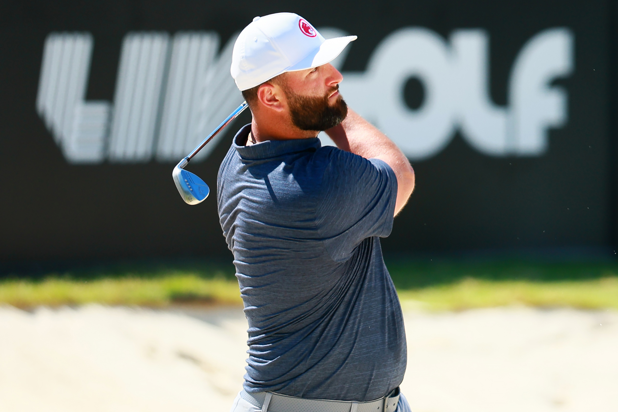 Jon Rahm in the finish position with a wedge after playing an approach shot into the green at a LIV Golf event, wearing LIV Golf Legion XIII clothing