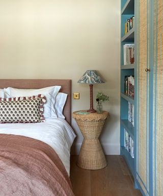 bedroom with light yellow wall and pink bedding, rattan nightstand