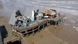 aerial view shows the damage by hurricane Beryl. Most of the roof is missing with the interior of the home exposed, some of it is completely flattened. It is located on a beach.