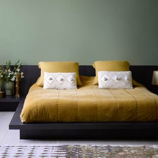 A green-painted bedroom with a low bed with mustard yellow bedding