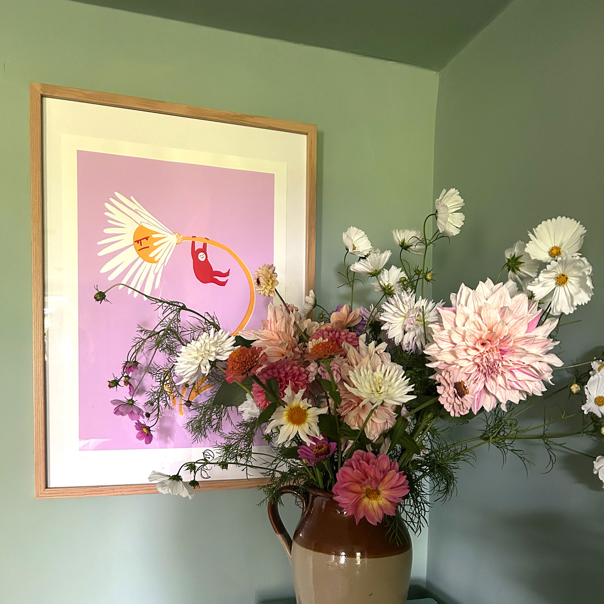 Vase of flowers in front of bright print hanging on green wall