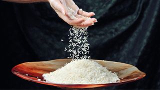 A woman drops a handful of rice into a bowl of rice