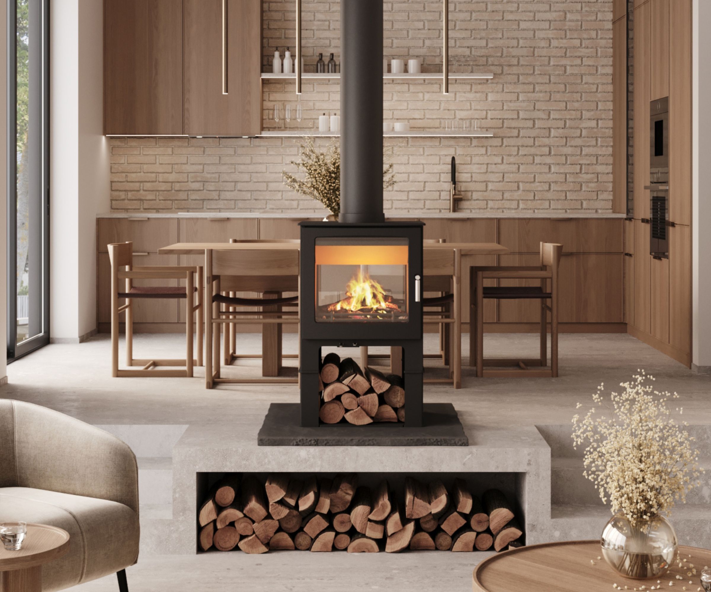 A sleek, double-sided log burner stands centrally in a modern open-plan kitchen and living space. The stove's black steel frame contrasts against soft, neutral tones, while its glowing flames warm both areas. Below, stacked logs add a functional yet rustic touch to the minimalist design, offering both heat and visual appeal.