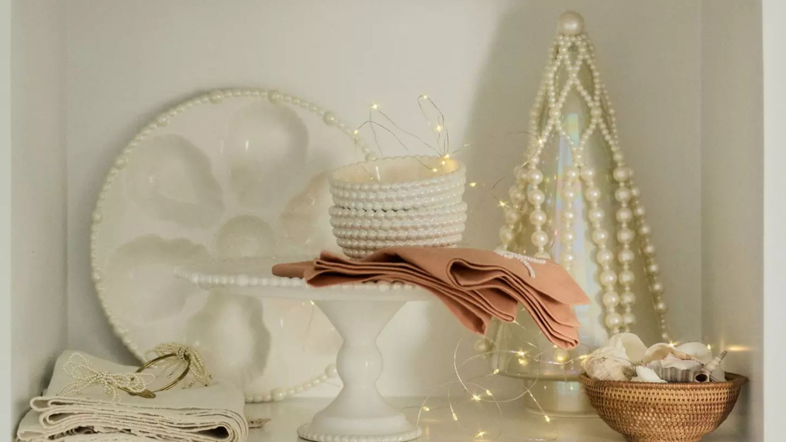 Shelf with pearl side plats, nut bowls, oyster plate and peach pink napkins, plus a glass and pearl Christmas tree ornament