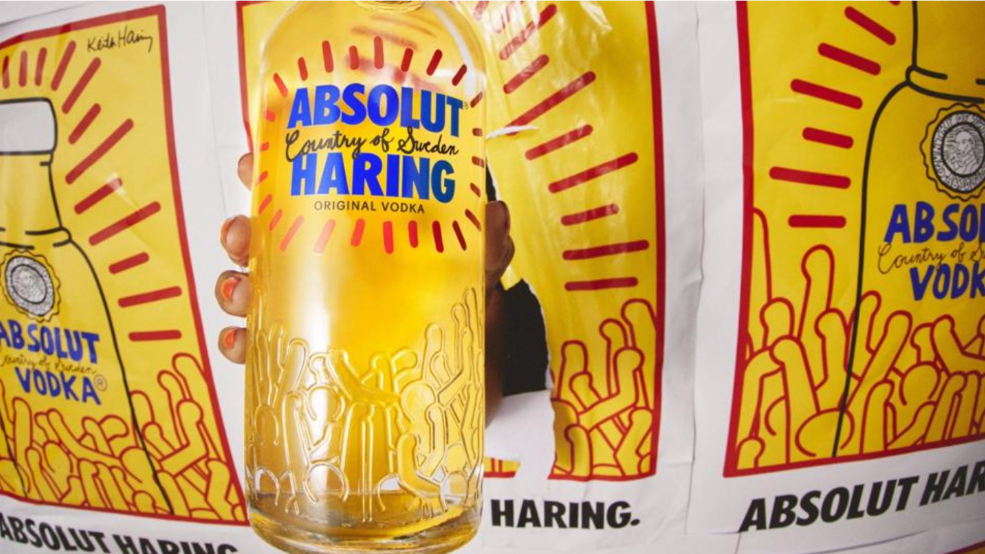 An image of the Absolut x Keith Haring limited edition bottle which is bursting out through a wall of limited edition keith haring posters and prints