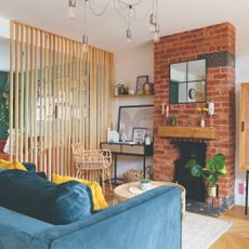 A living room with an exposed-brick fireplace and a WFH station separated into zones with a slatted screen