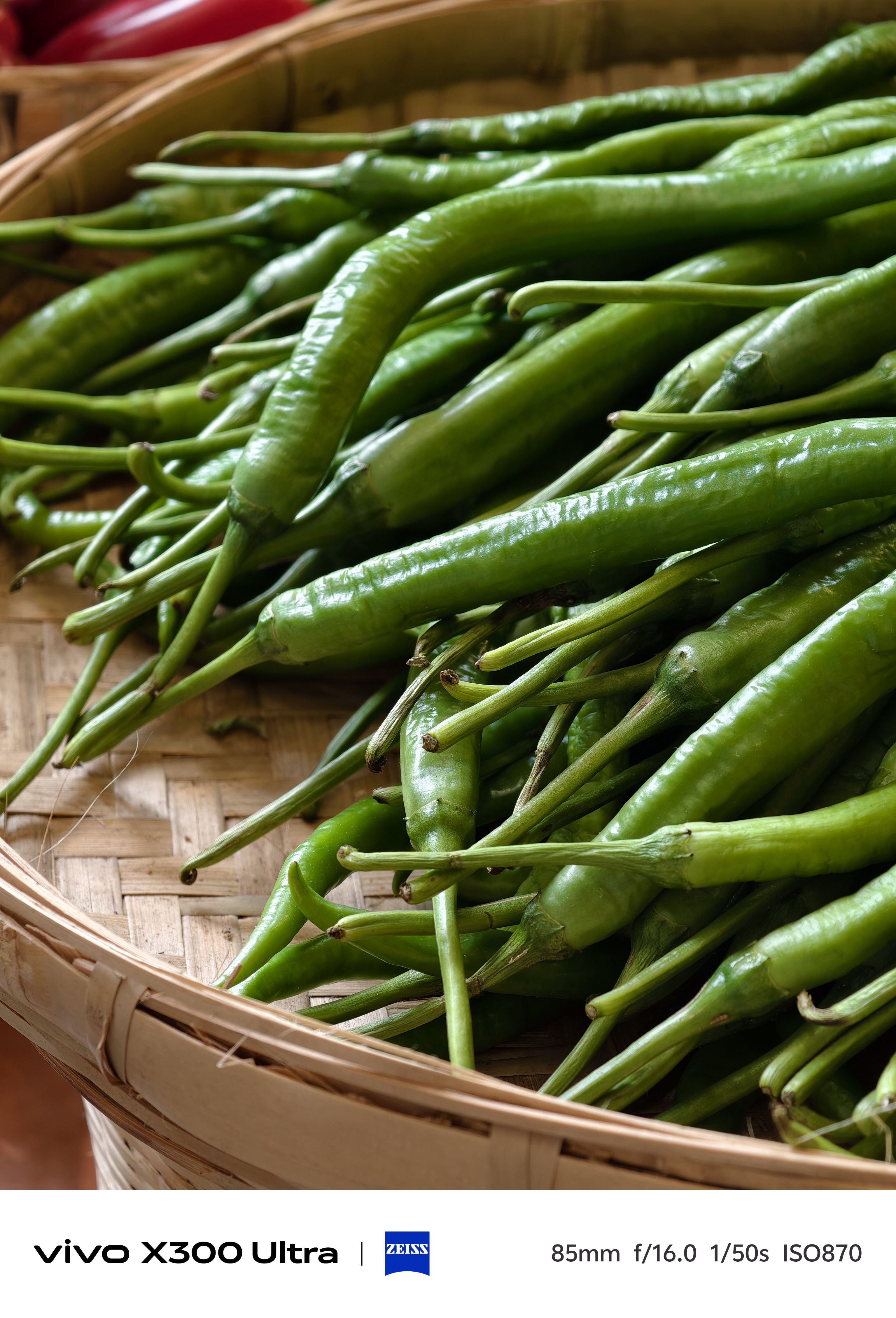 A top-down, close-up shot filling the frame with fresh, vibrant green chili peppers piled neatly inside a woven bamboo basket.