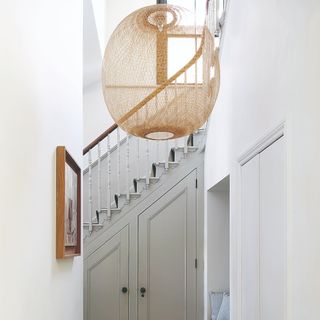 A narrow white hallway with a grey staircase at the end and an oversized rattan pendant light