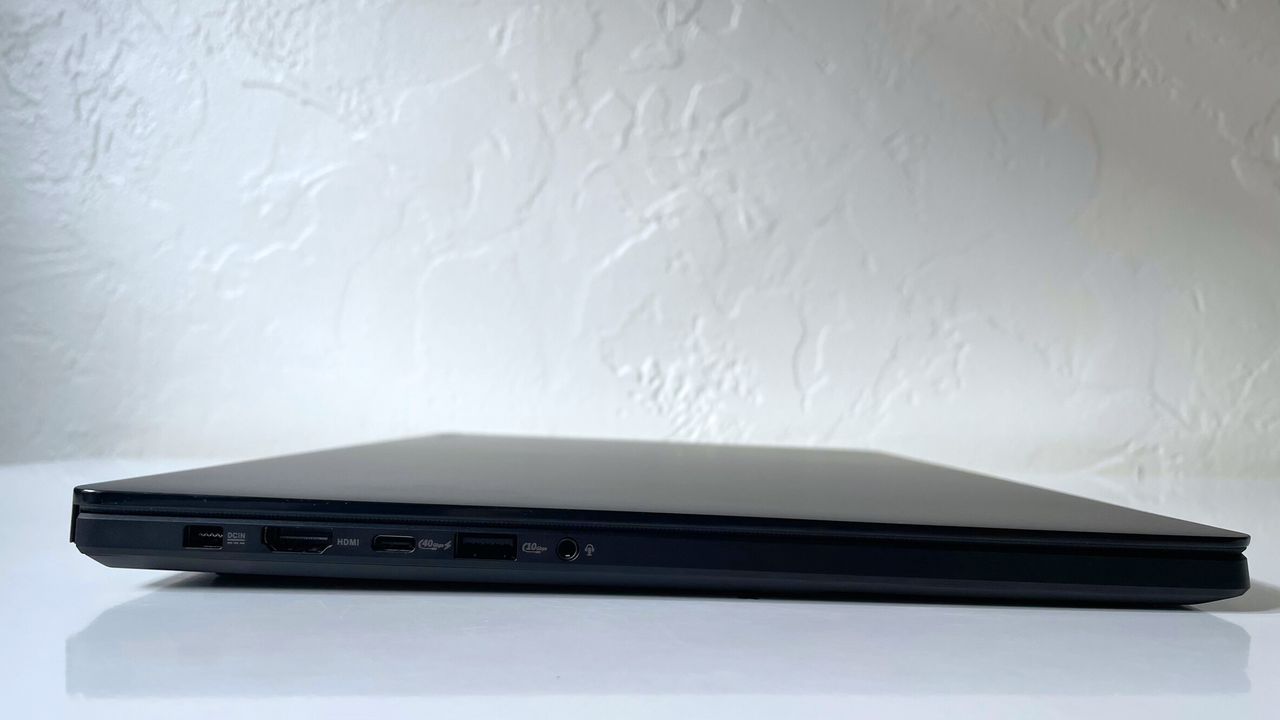 Close up of the ports on the side of a black laptop on top of a white surface against a white wall.