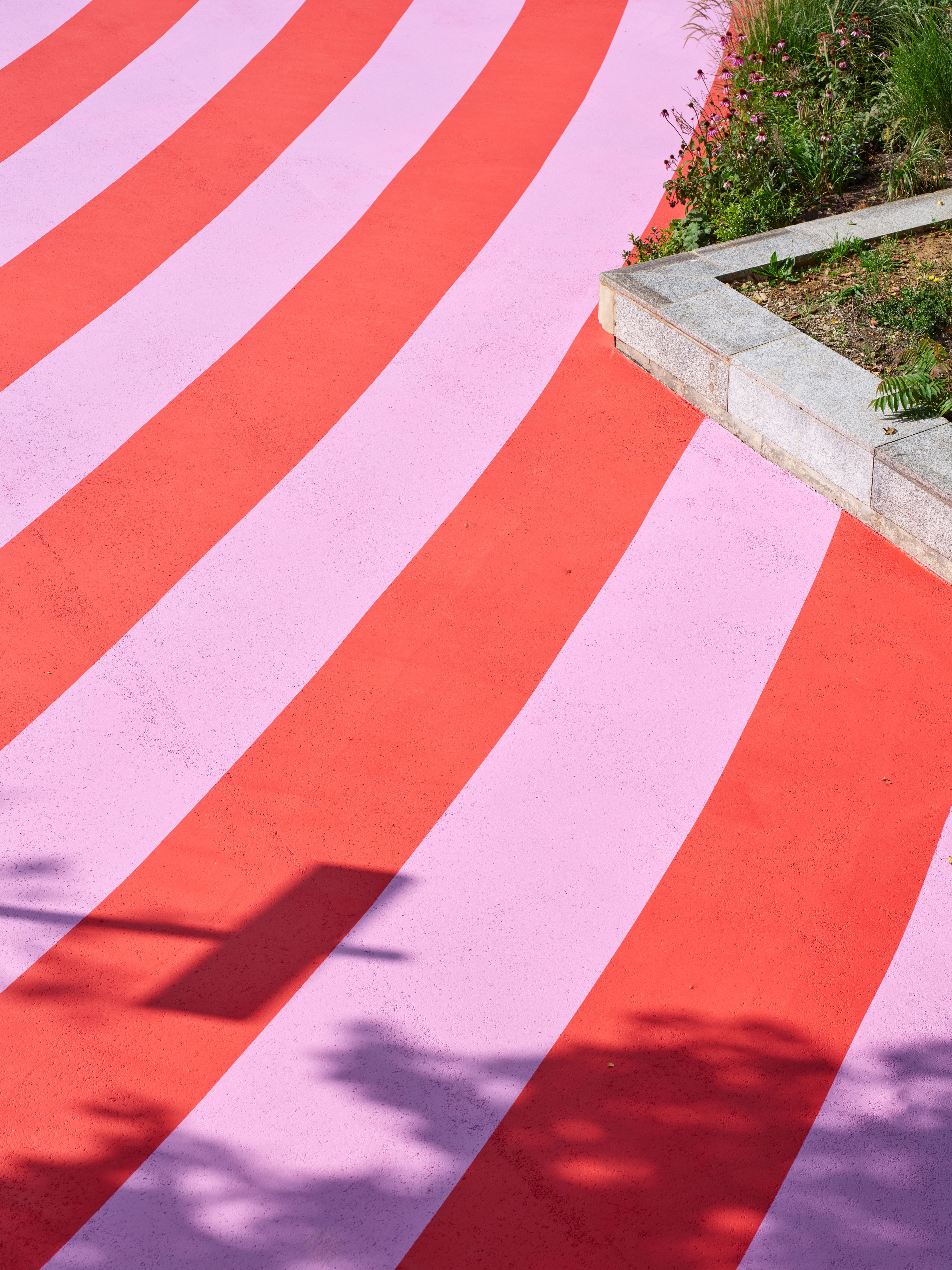 Aerial view of a colorful, abstract mural in tones of pink, red, green, yellow, and blue as seen up close on a sunny day.