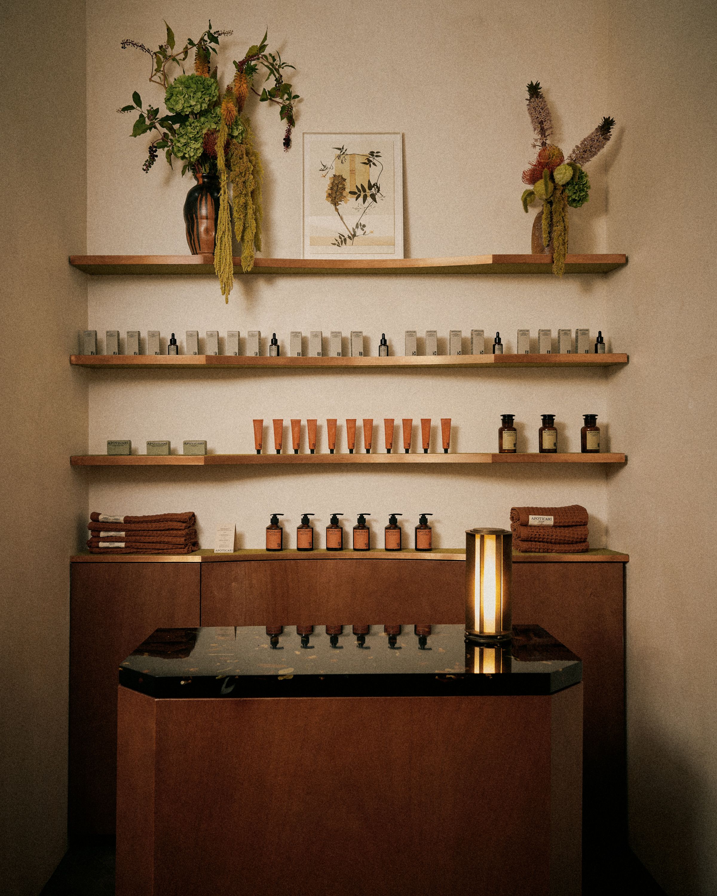 A naturally lit teahouse bar and dining room cast from resin filled with florals, decorated with bronze surfaces mixed with wood and beige plasters, along with wooden stools.