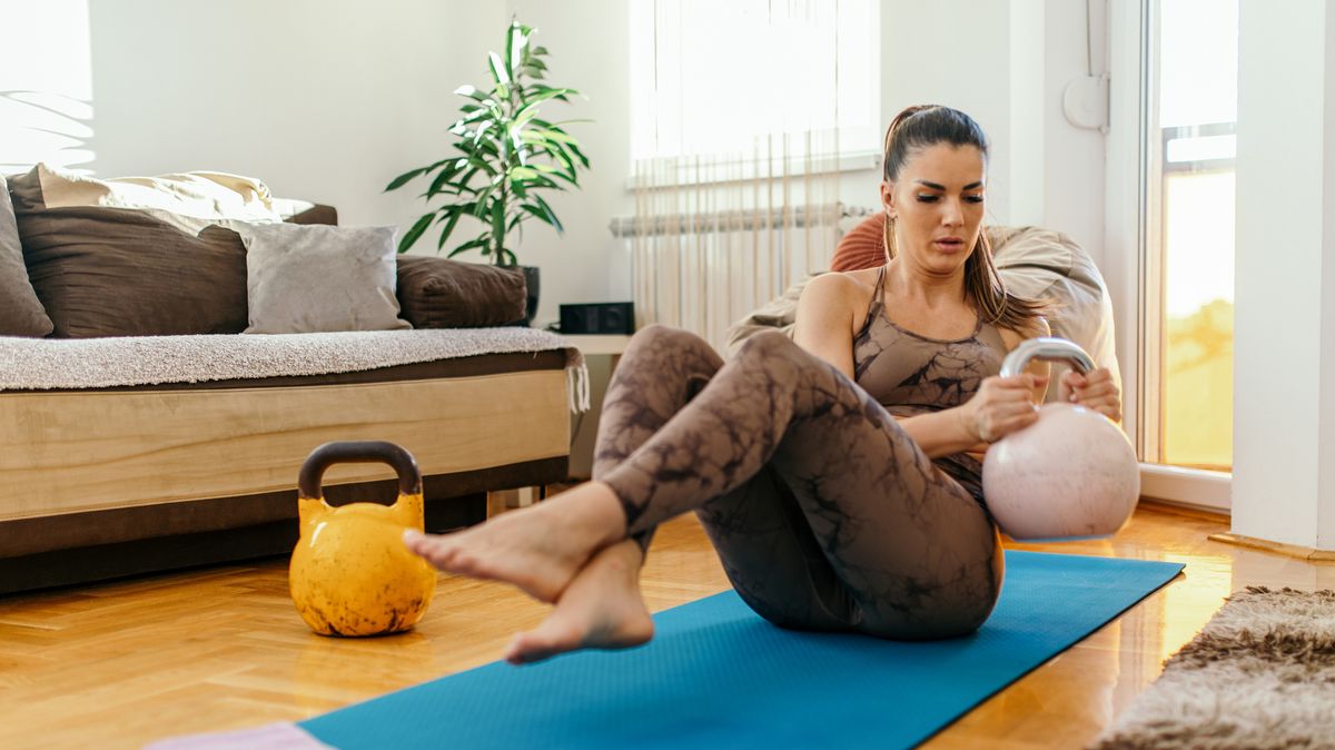 Woman performs Russian twist core exercise at home using a kettlebell