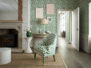 A white and green living room featuring green and white patterned wallpaper and matching armchair in front of a stone fireplace with large gilt mirror.