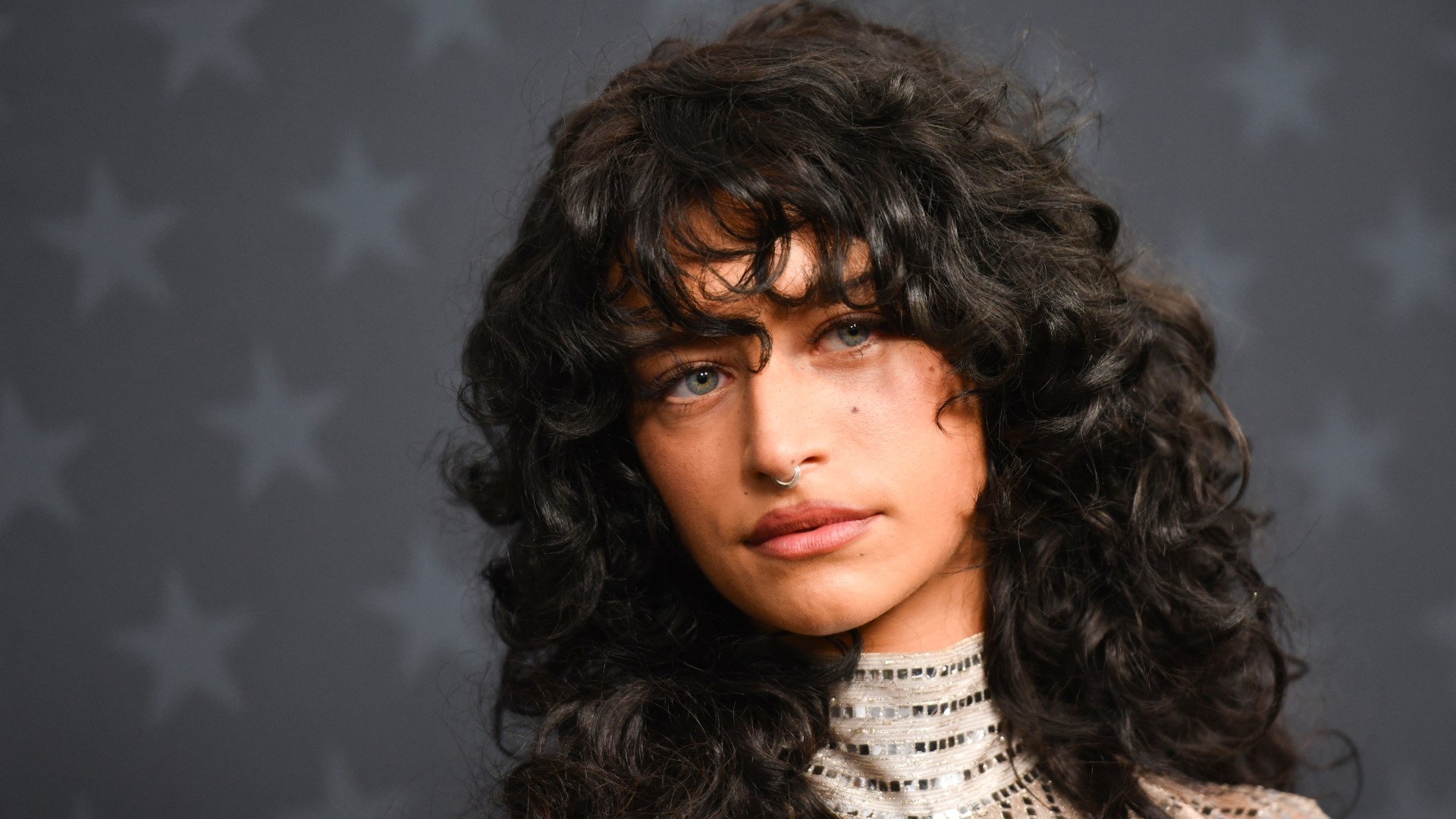 a white woman with curly black hair poses on a red carpet in front of a dark background